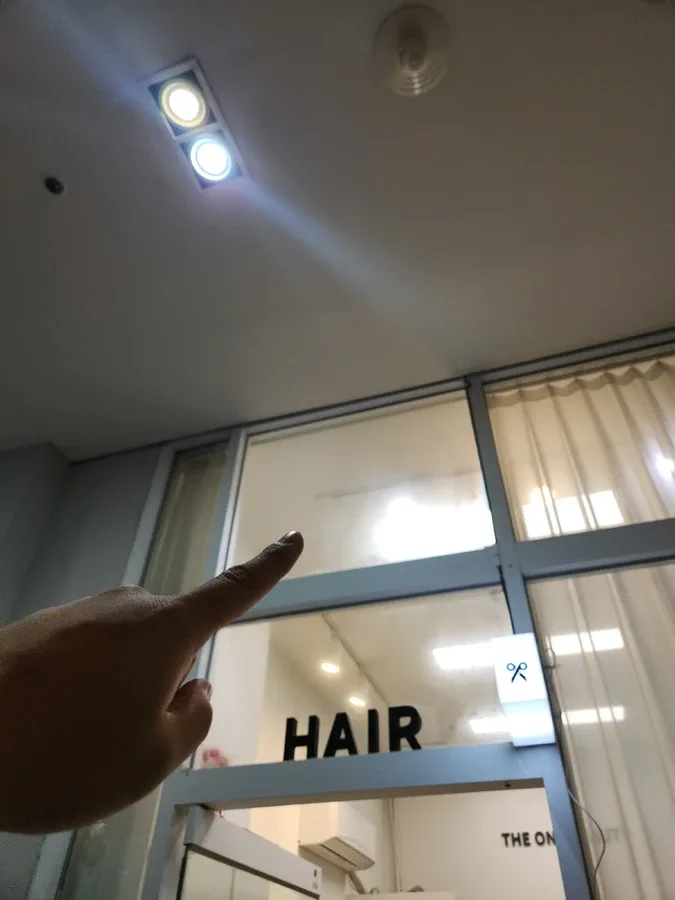 유리 출입문 상단 환기 위치를 손으로 가리키는 미용실 입구