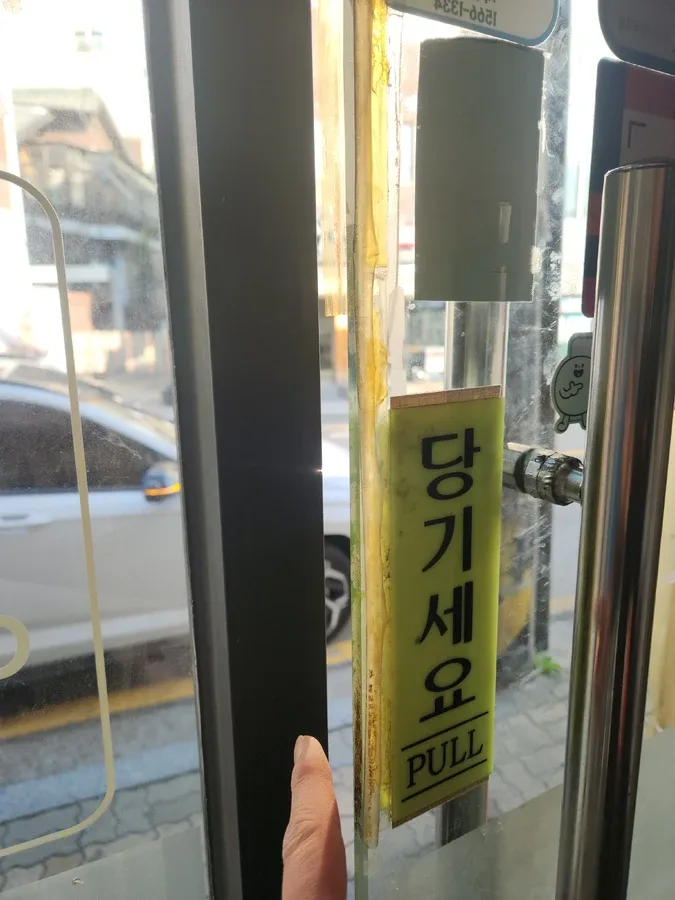 미용실 같은 통유리 매장 출입문 옆 프레임과 손잡이 주변을 확인하는 모습