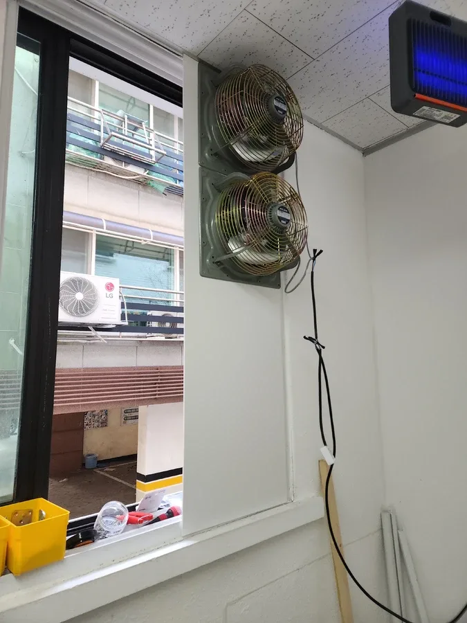 창가에 환풍기 두 대를 세로로 설치한 건물 창문