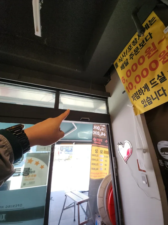매장 출입문 위쪽 채광창을 가리키며 환풍기 설치 위치를 확인하는 모습